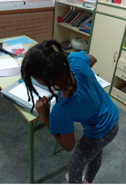 Niña perforando hojas durante el proceso de montaje de su cuaderno de trabajo.